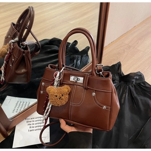 Detail of dark brown vintage handbag with white stitching and plush bear charm decoration