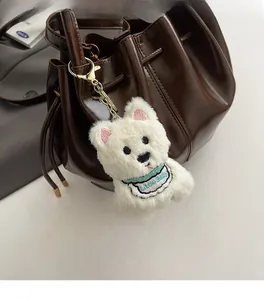 Gros plan d'un bijou de sac chien en peluche blanche sur un sac seau en cuir marron