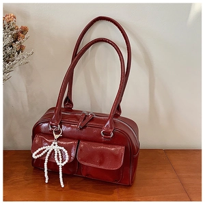 Détail du sac Boston rouge foncé avec charm nœud perlé et poches sur bois