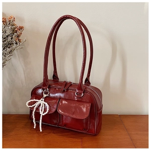Détail d'un sac Boston rouge foncé en cuir verni avec pendentif nœud en perles sur bois