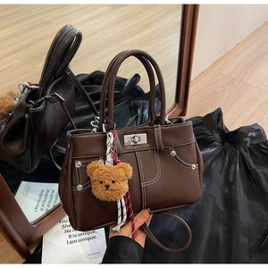 Detail view of dark brown vintage handbag with white stitching and plush bear charm