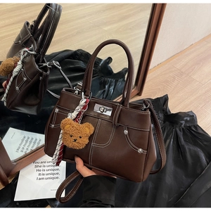 Detail of dark brown tote bag with contrast stitching, silver lock and plush bear charm