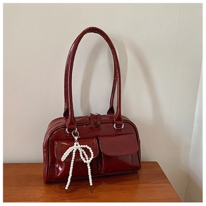 Détail du sac Boston rouge foncé brillant montrant le cuir verni et le charm nœud en perles