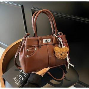 Close-up of brown faux leather handbag with contrast stitching and teddy bear charm