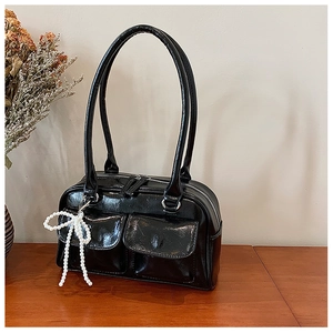 Détail du sac Boston en cuir verni noir avec zips argentés et breloque en perles
