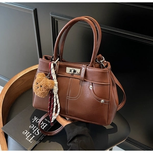 Detail of vintage brown leather handbag with contrast stitching, scarf and bear charm