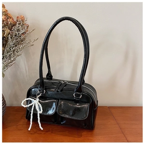 Détail du sac Boston noir brillant avec poches avant et breloque nœud en perles