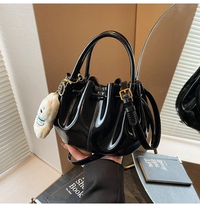 Détail du sac seau en cuir verni noir avec bords plissés et finitions dorées