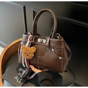 Detail of brown vintage PU leather handbag with white stitching and bear charm on black chair