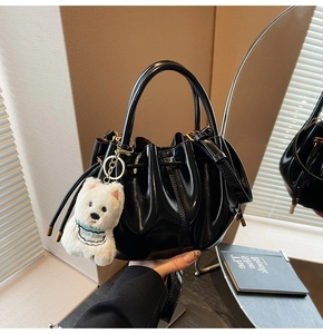 Détail du sac seau plissé noir avec finition brillante et breloque peluche chien blanc