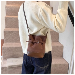Detail of dark brown matte bucket bag with leather strap buckle on model on a staircase
