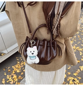 Sac seau plissé en cuir verni marron avec charme en peluche sur feuilles d'automne