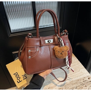 Close-up of brown pebbled leather handbag with metallic studs, scarf, and bear charm