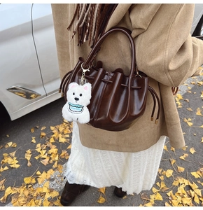 Détail du sac à main plissé en cuir verni marron foncé avec un charme chien en peluche