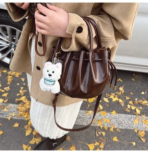 Détail du sac seau plissé marron foncé brillant avec pendentif ours en décor d'automne