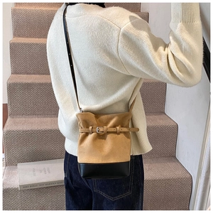 Model wearing a two-tone suede bucket bag in camel and black on a carpeted staircase
