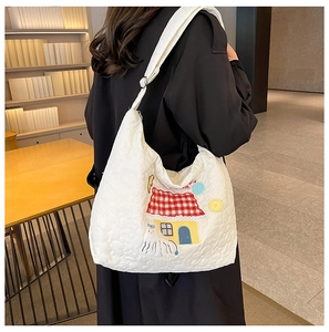 Close-up of quilted white nylon tote bag featuring cute cartoon house patch and buttons