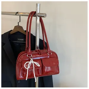 Détail du sac Boston en cuir verni rouge avec nœud en perles et poches frontales