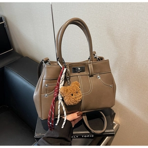 Detail of a brown vintage handbag featuring a bear charm and elegant contrast stitching