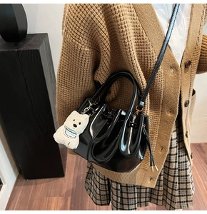 Détail d'un sac seau en cuir verni noir brillant avec plis et breloque ours en peluche