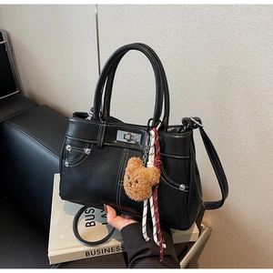 Detail of vintage black leather handbag with white stitching and bear charm