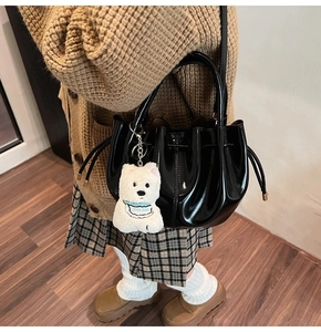 Détail du sac seau noir brillant plissé avec un charmant pendentif en peluche blanc