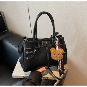 Detailed view of black faux leather handbag with contrast white stitching and bear charm