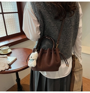 Gros plan d'un sac seau vintage marron avec breloque ours en peluche dans un décor automnal