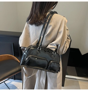 Close-up of black glossy leather shoulder bag with side zip pockets shown on model