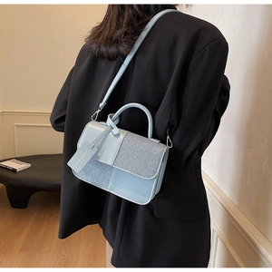 Détail du sac bandoulière bleu clair avec un design épissé en cuir mat et paillettes argentées