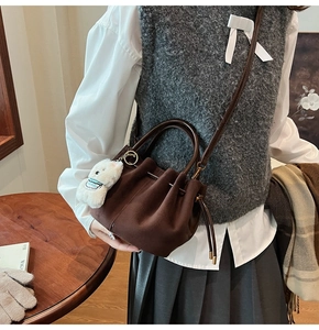 Détail du sac seau en daim marron foncé avec plis et pendentif chiot en peluche