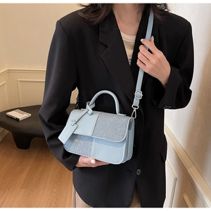 Détail du sac bandoulière bleu clair avec patchwork texturé et étiquette décorative