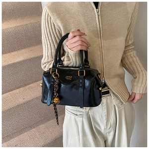 Detail of black glossy leather Boston bag with gold bell pendant and logo lettering
