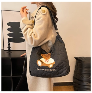 Detail of black quilted shoulder bag with brown plush bear and embroidery on a model