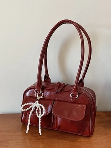 Sac Boston bordeaux avec poches latérales et breloque nœud perlé sur une table en bois