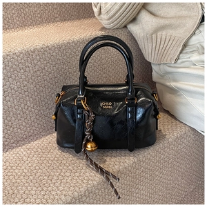 Detailed macro view of the glossy black leather texture and gold logo on a Boston handbag