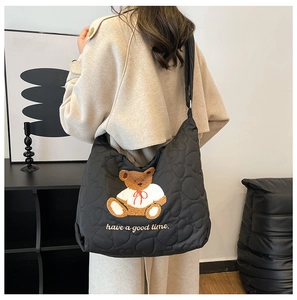 Detail of heart-quilted black nylon tote featuring cute teddy bear and slogan embroidery