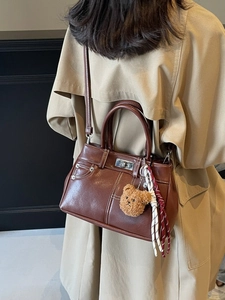 Retro brown PU leather handbag with shoulder strap and bear charm worn on a trench coat