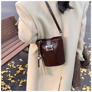 Détail du sac seau marron foncé avec boucle argentée sur des feuilles d'automne