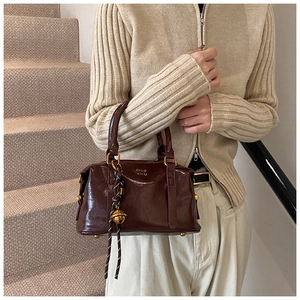 Detail of vintage brown shiny leather handbag with gold logo and decorative bell charm