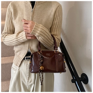 Close-up of dark reddish-brown glossy Boston bag with gold hardware and rope charm detail