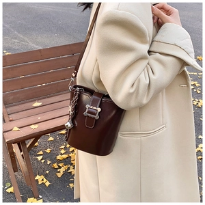 Détail du sac seau en cuir marron avec boucle métallique ondulée et chaîne dorée