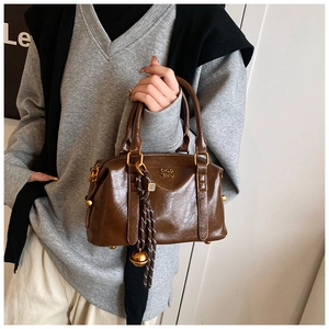 Detail of a brown Boston handbag featuring dual handles and a golden metal ball charm