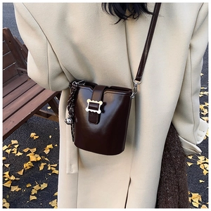 Détail du sac seau marron foncé avec boucle argentée ondulée et ornement de bandoulière