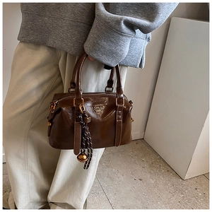Detail view of brown vintage Boston bag featuring gold letters and braided rope pendant