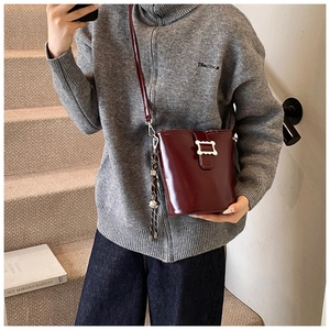 Détail du sac seau bordeaux en cuir brillant avec boucle dorée et pompon
