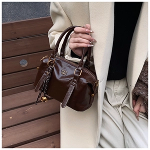 Detail of dark brown glossy leather Boston bag with metal zipper and round pendant charm