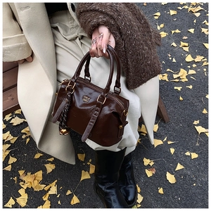 Detail of dark brown glossy Boston bag featuring gold metal logo and decorative silk scarf