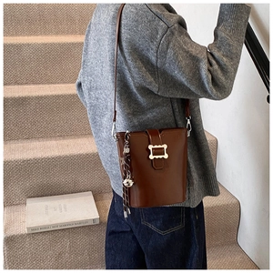 Sac seau en cuir marron foncé porté en bandoulière par un mannequin en décor intérieur