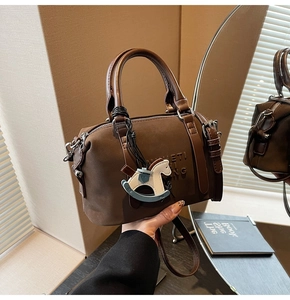Detail of a brown suede Boston bag featuring double handles and a blue horse charm